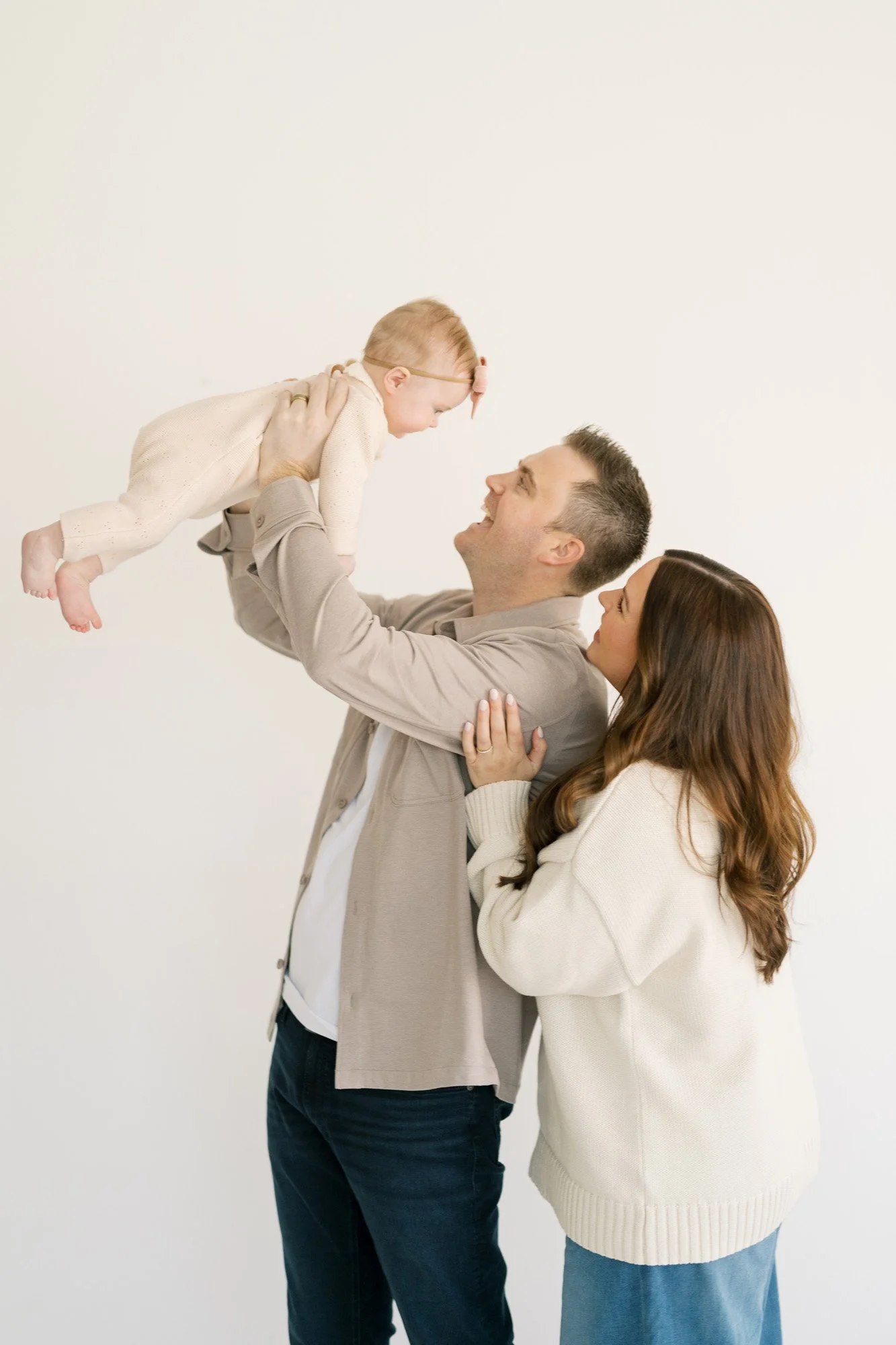 Dad tossing baby gently while mom looks on in studio