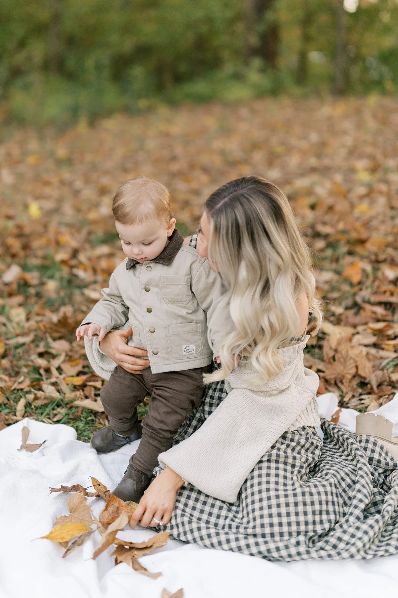 Mother and toddler son on a blanket in a park with lots of fallen leaves in the autumn