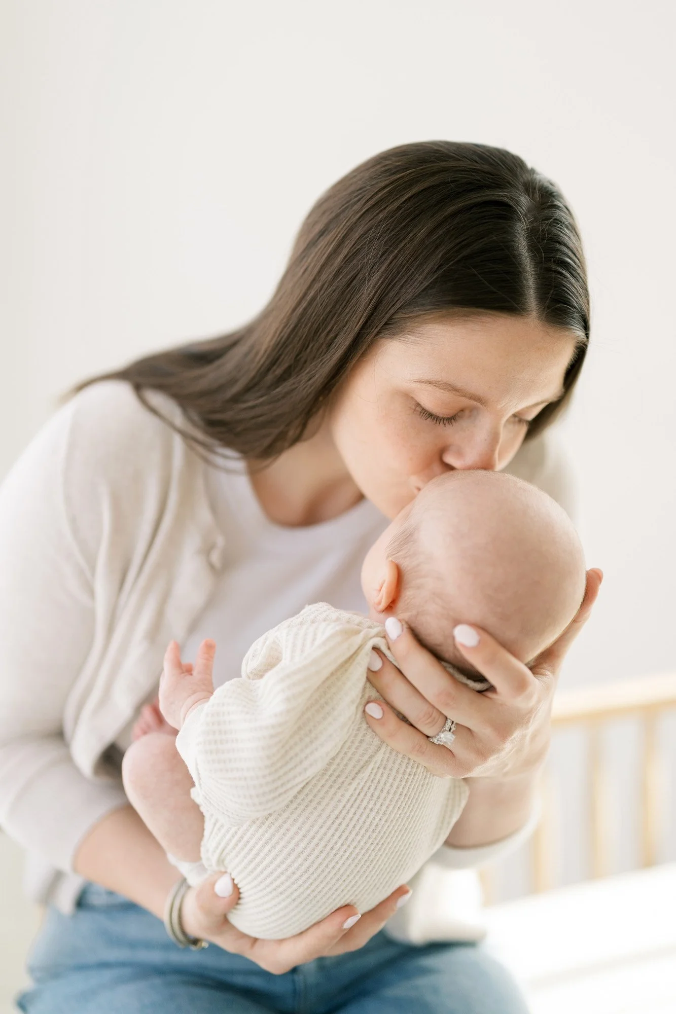 mother kissing a baby on the forehead in beautiful natural light studio