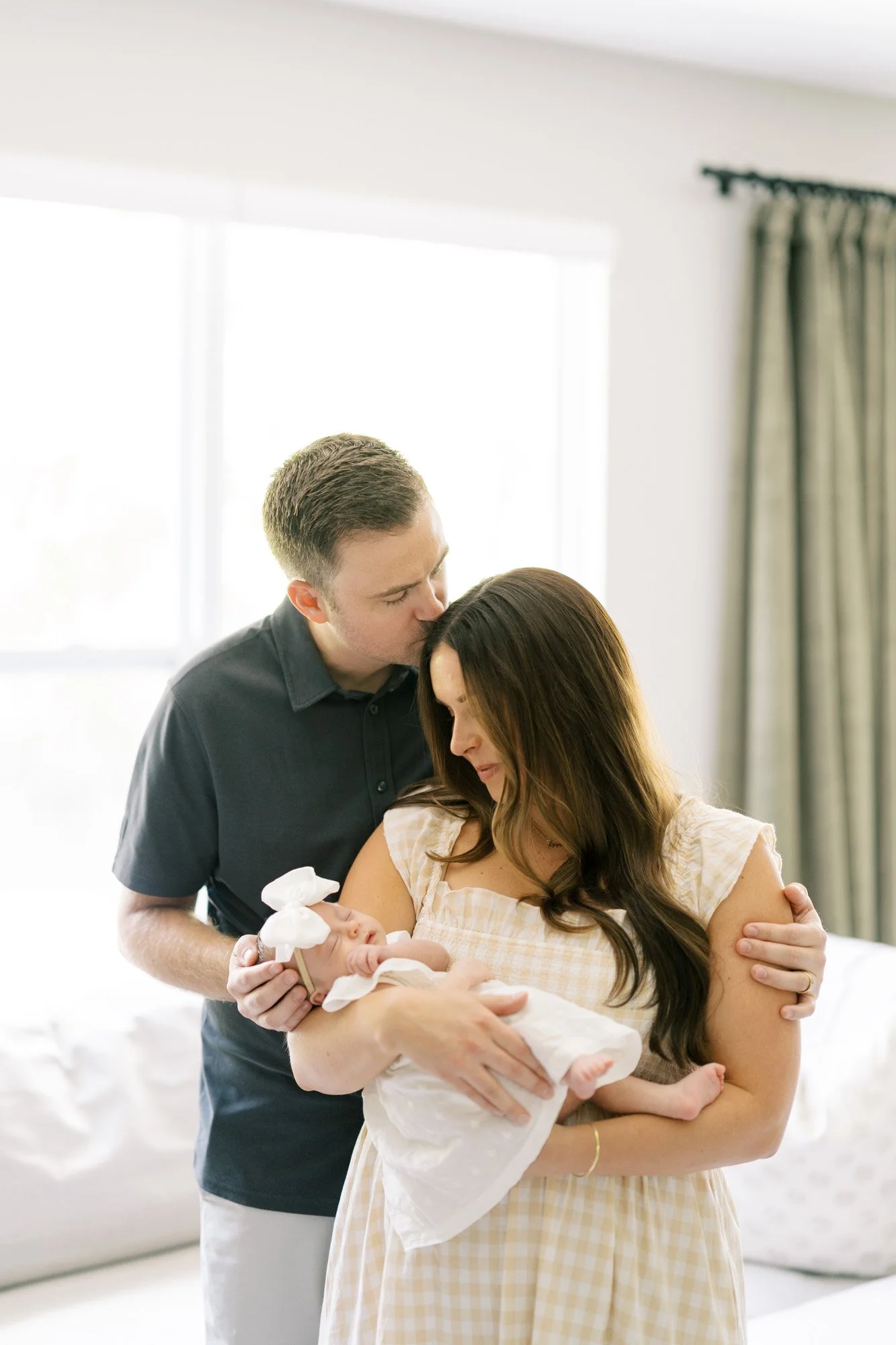Dad kissing mom on head while mom holds and looks at newborn baby