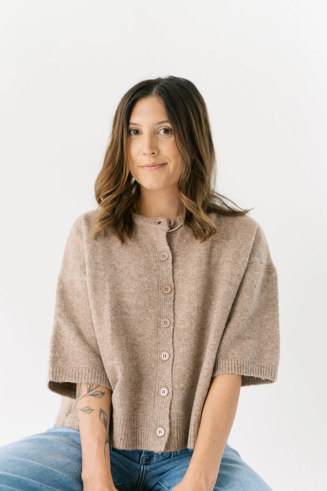 Tristan sitting on a stool in Singleton Studio, wearing brown soft sweater and smiling