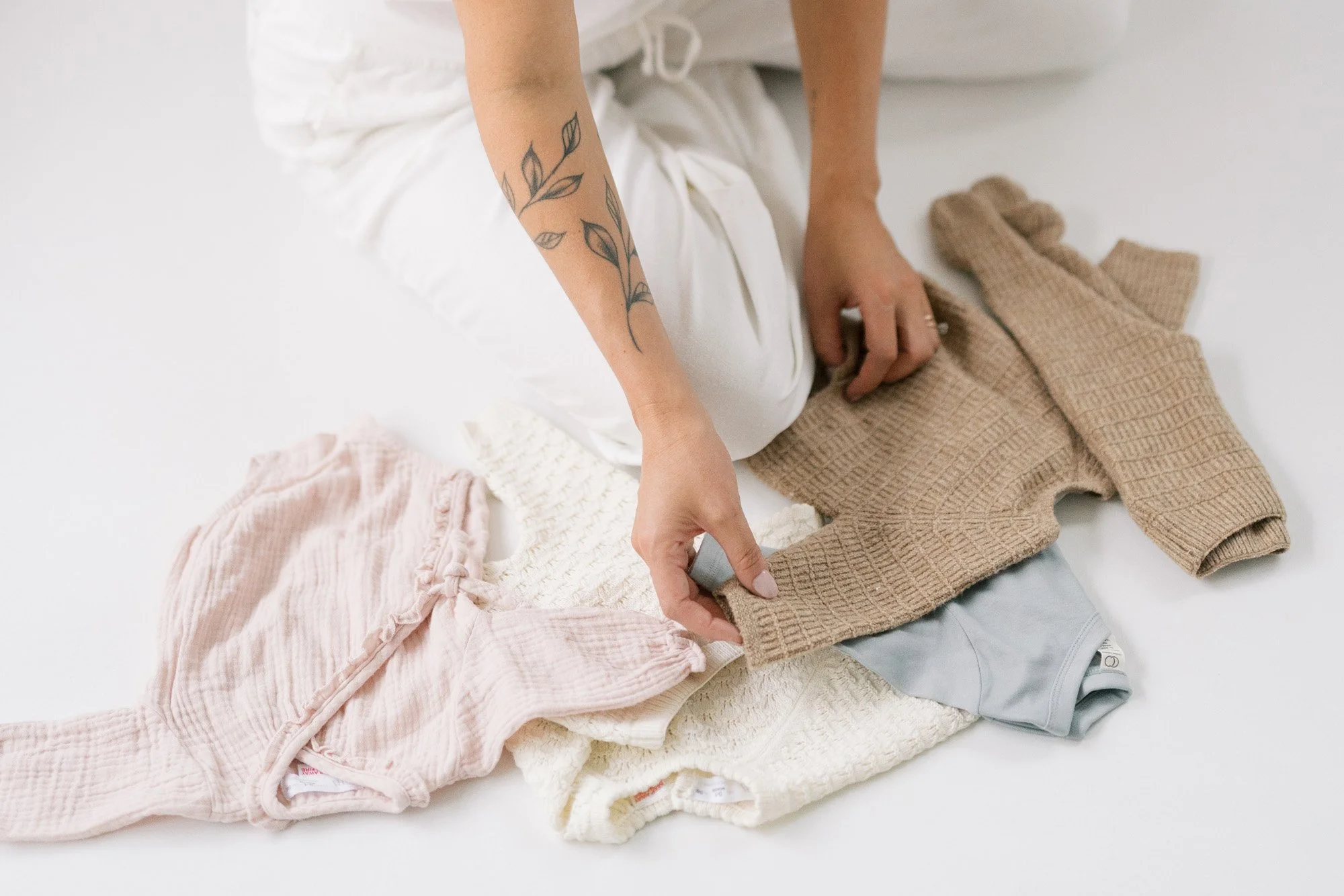 Hand holding the sleeve of a knitted infant sweater on a pile of other infant clothes