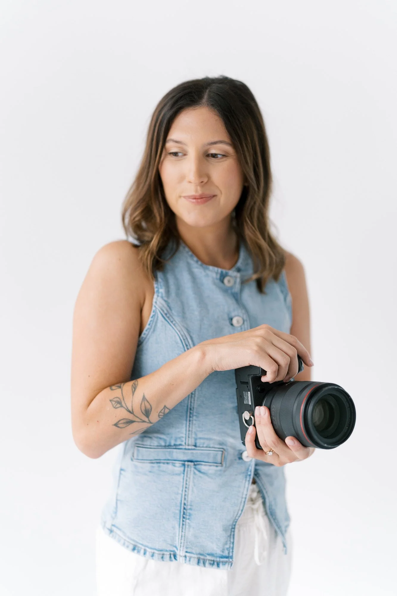 Tristan in a sleeveless chambray top and white pants in her studio, holding her canon camera