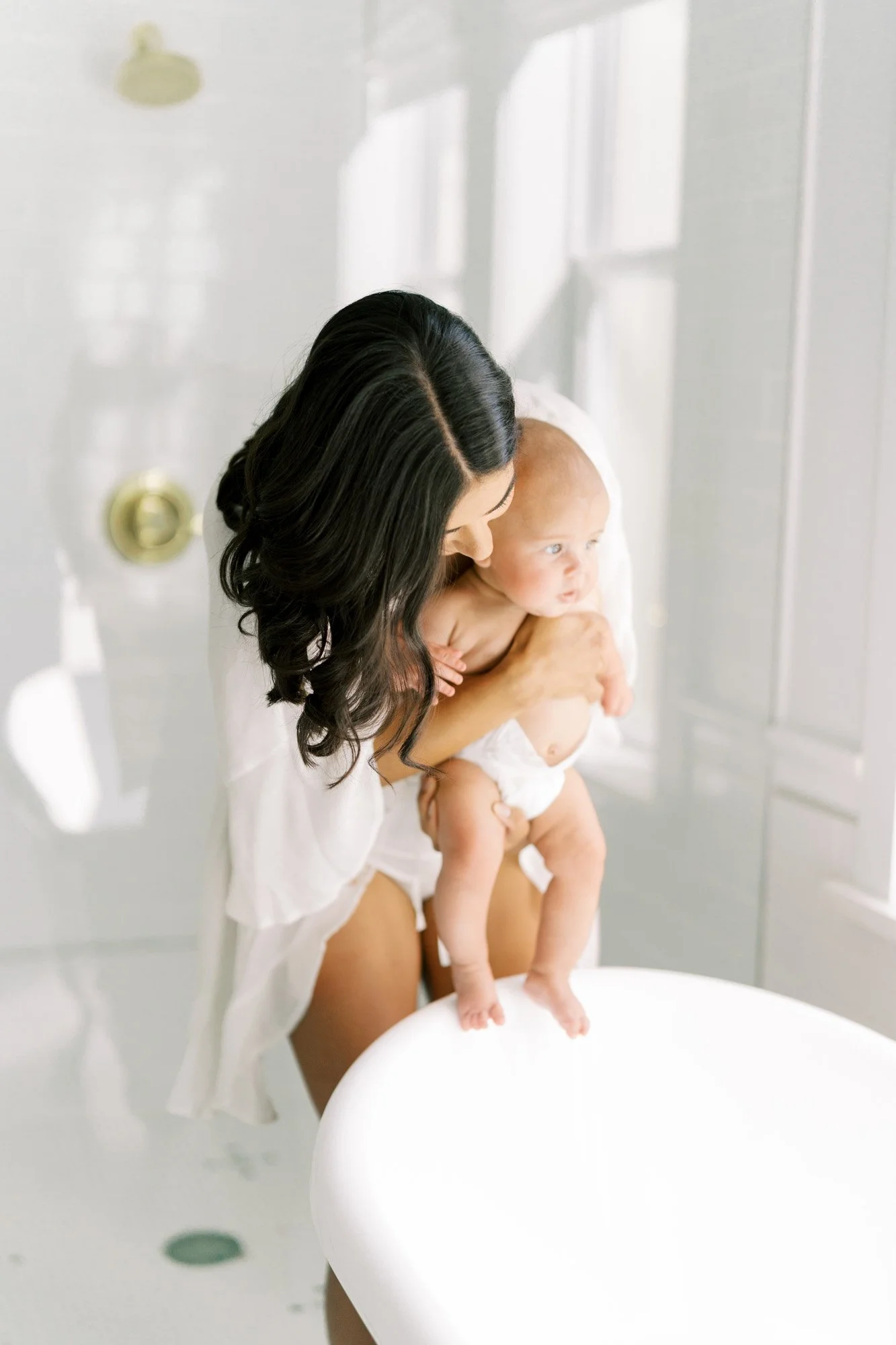 Mother holding newborn near window by Tristan Singleton Photography