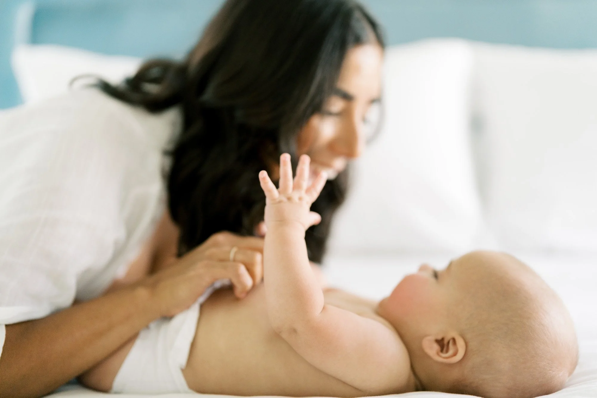 indoor portrait of mother looking over her newborn baby on a bed in a blue room