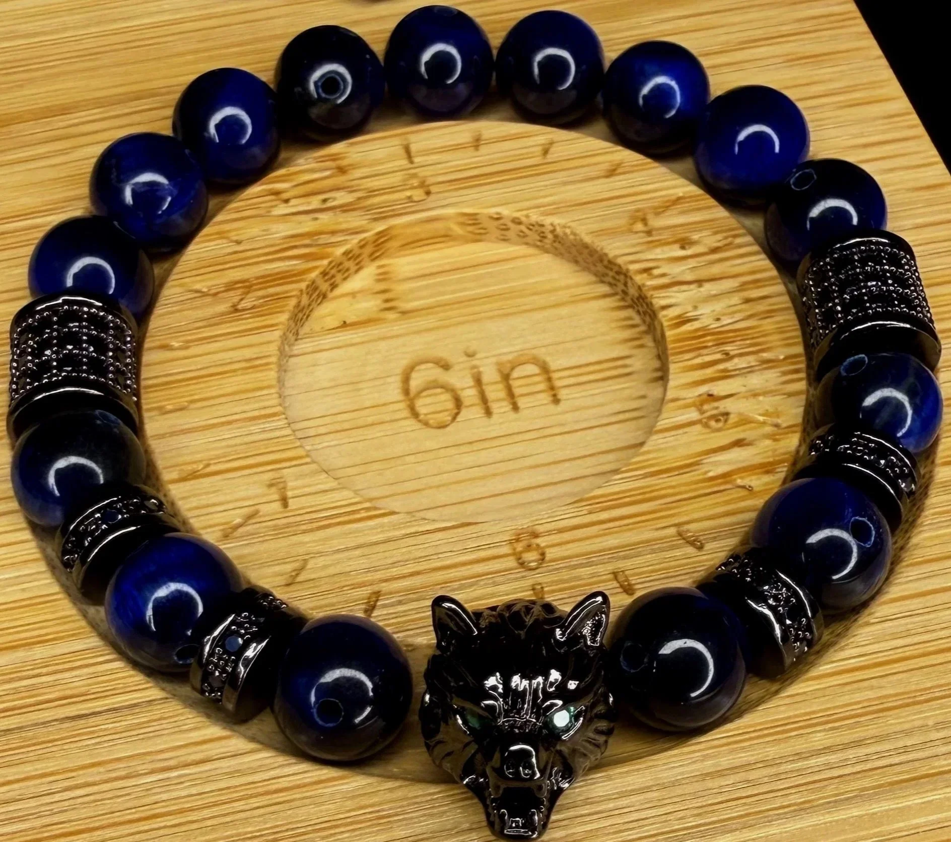 Blue beaded bracelet with black metal wolf head charm on a wooden surface with the word 'gin' carved into it.