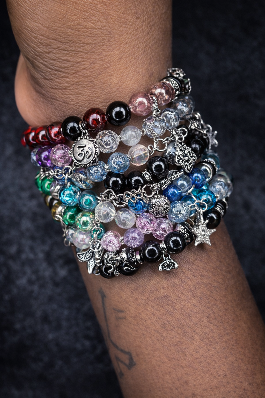 A close-up of a person's wrist adorned with multiple colorful beaded bracelets with charms, including stars, hearts, and other symbols, against a dark background.