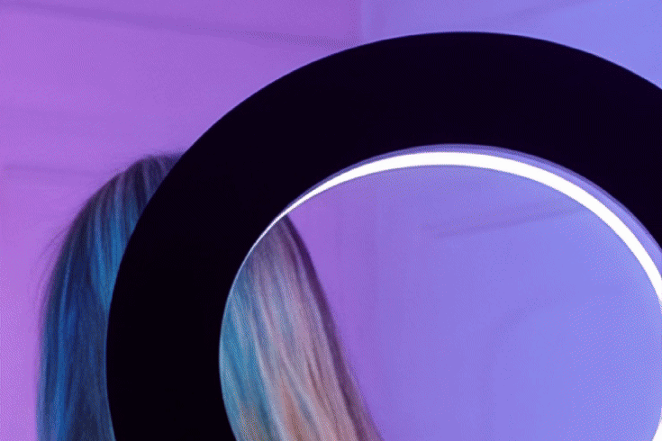 Close-up of a neon-lit circular ring with a colorful background of light purple and blue hues.