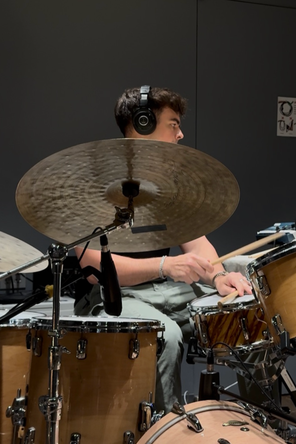A young man wearing headphones playing a drum set in a recording studio.