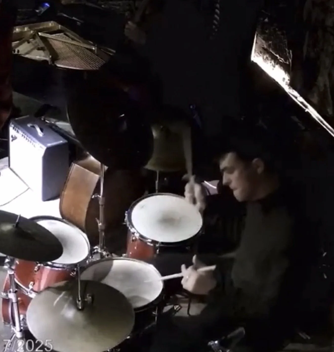 A person playing a drum set in a dimly lit room with musical equipment.
