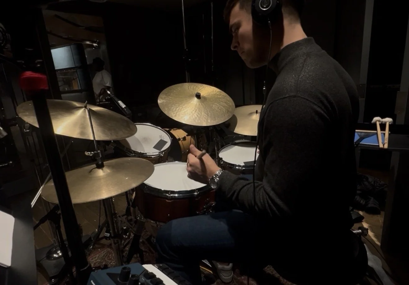 A person wearing headphones playing a drum set in a music studio.
