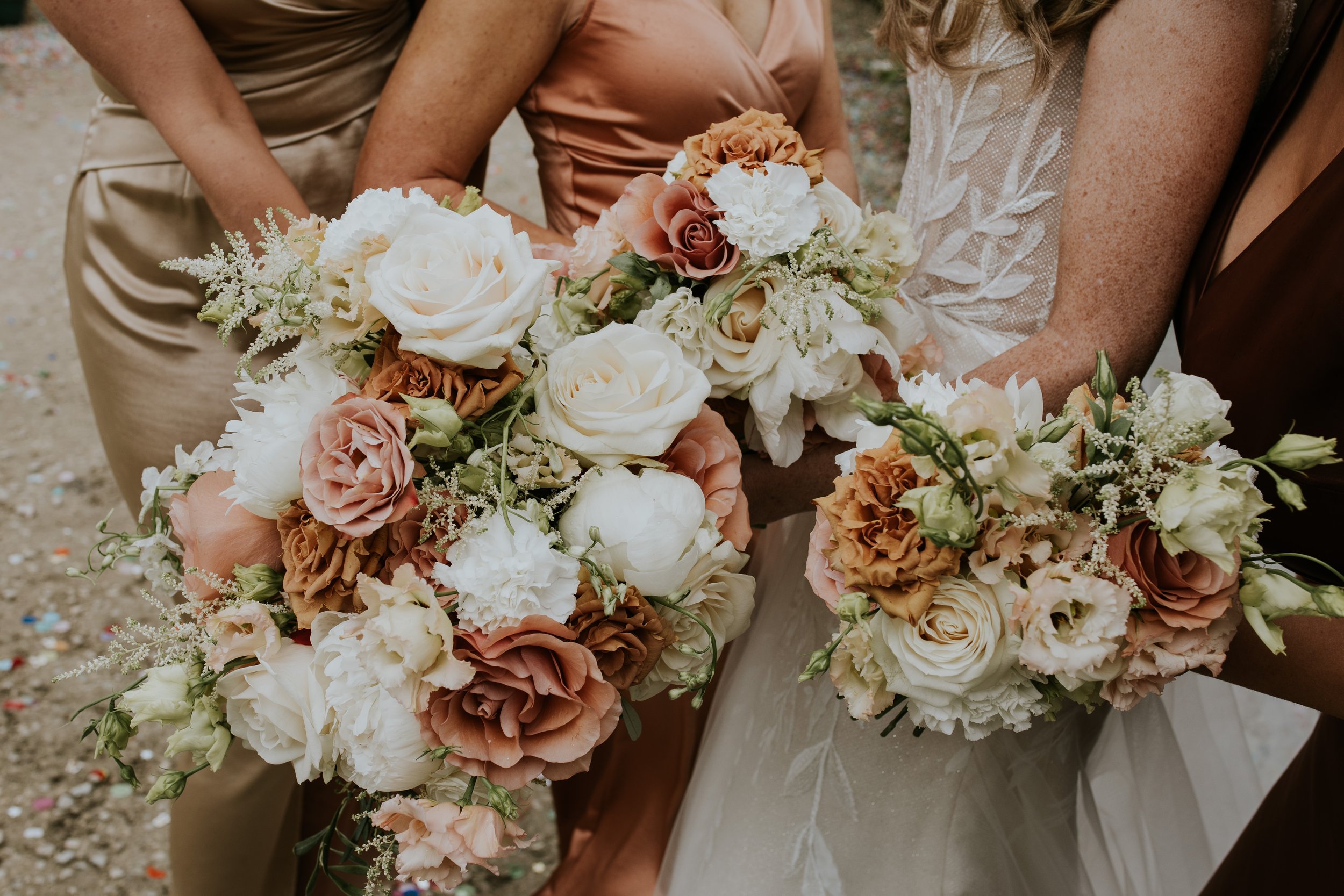 Close-up of four women holding colorful bouquets of roses and other flowers, standing outdoors.
