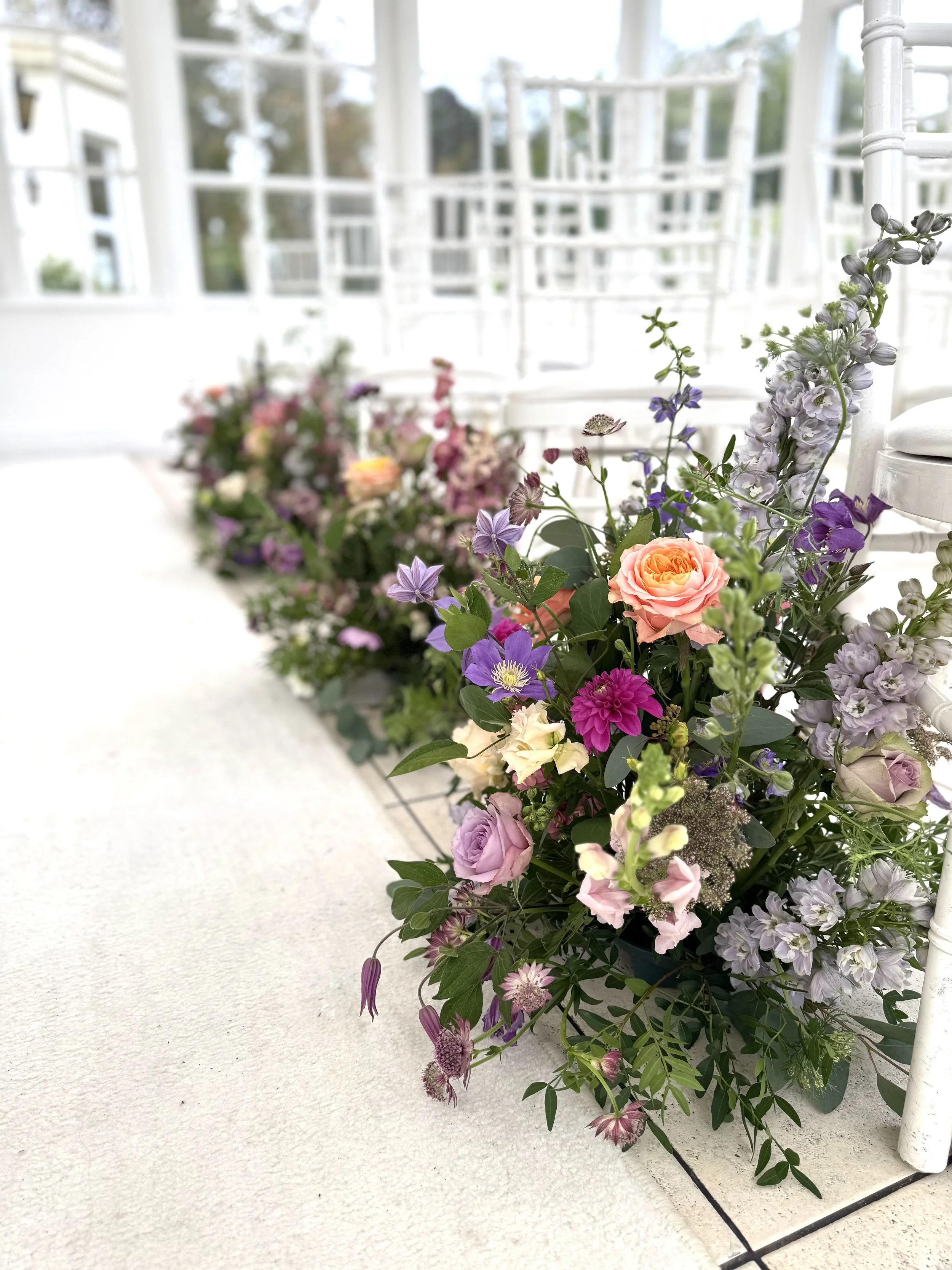 Colorful floral arrangements with pink, purple, peach, and white flowers on a white tiled porch or balcony railing.