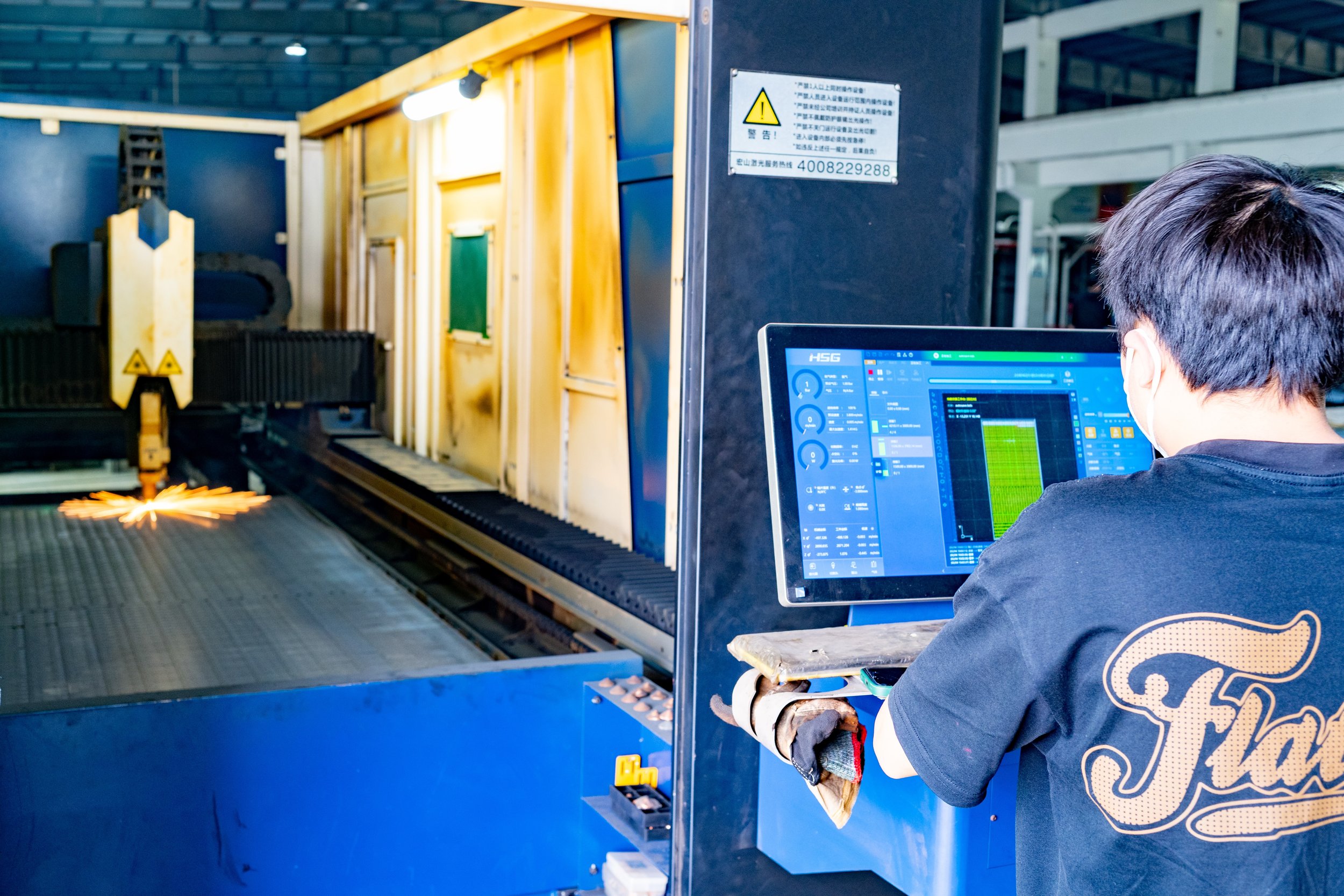An industrial worker operating a computer to monitor a CNC machine that welds metal parts in a factory.