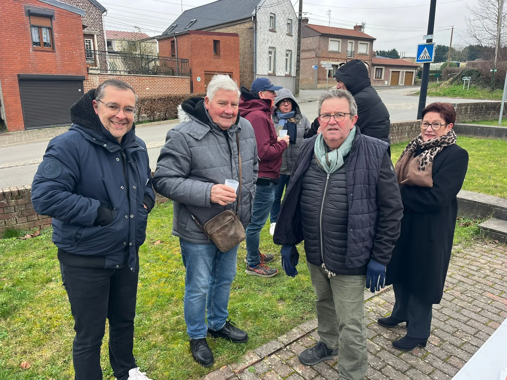 Groupe de personnes avec des vêtements d'hiver, certaines tenant des gobelets, se rassemblant dans un espace extérieur résidentiel.