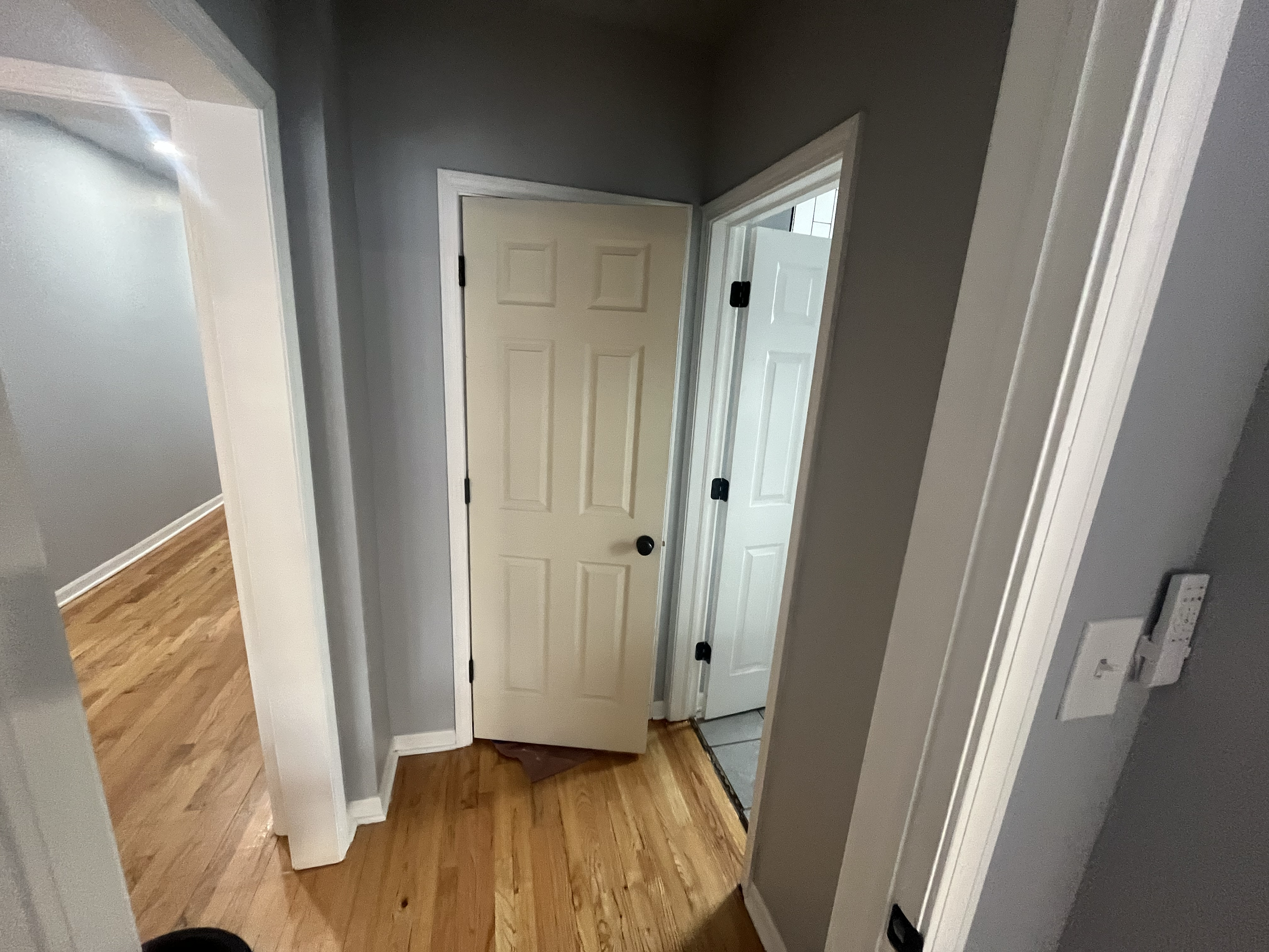 View of the interior of a house showing a wooden floor, gray walls, and an open door leading to a small tiled entryway.
