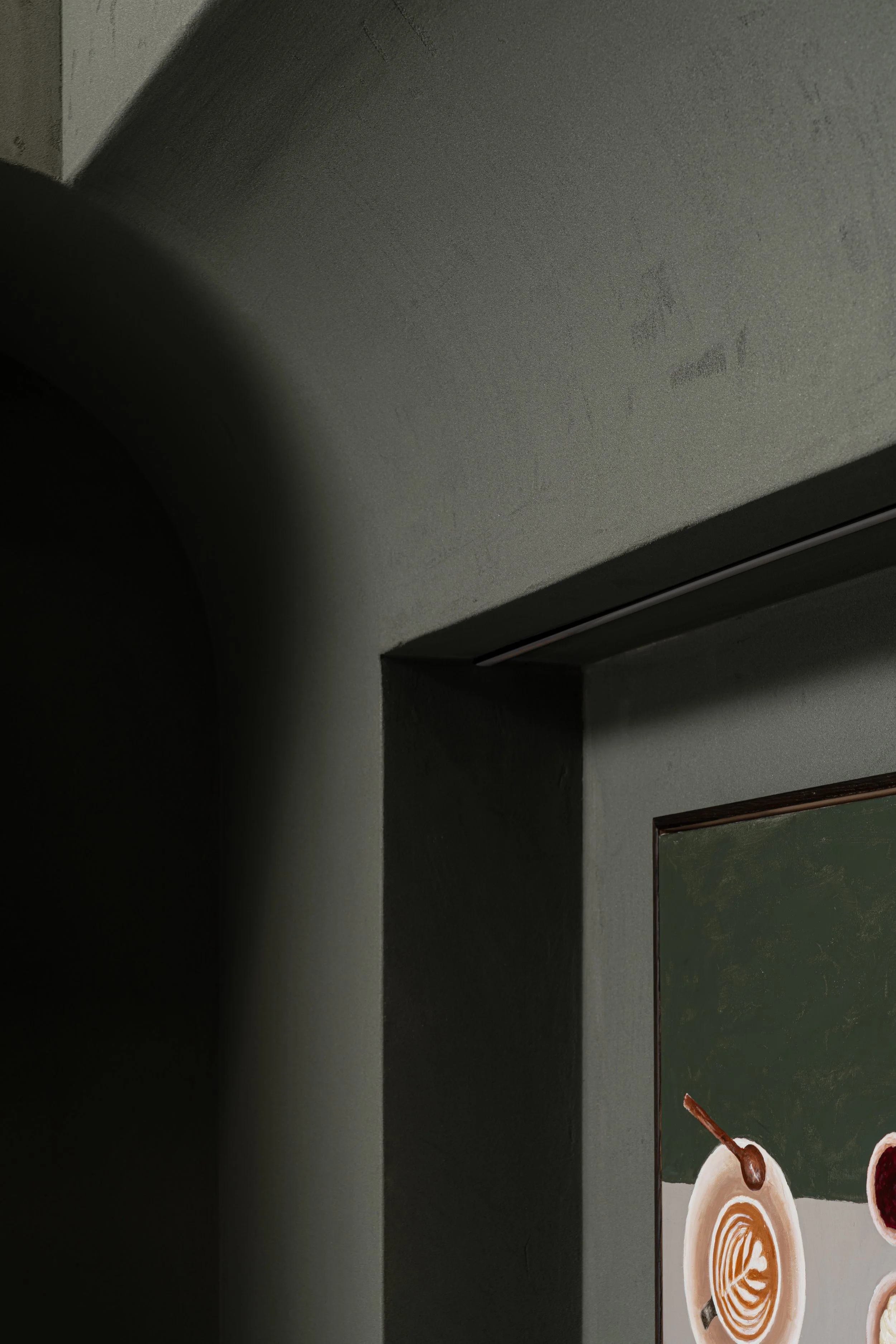 Part of a framed picture of coffee drinks on a dark green wall, with a shadow cast by a nearby wall or object.