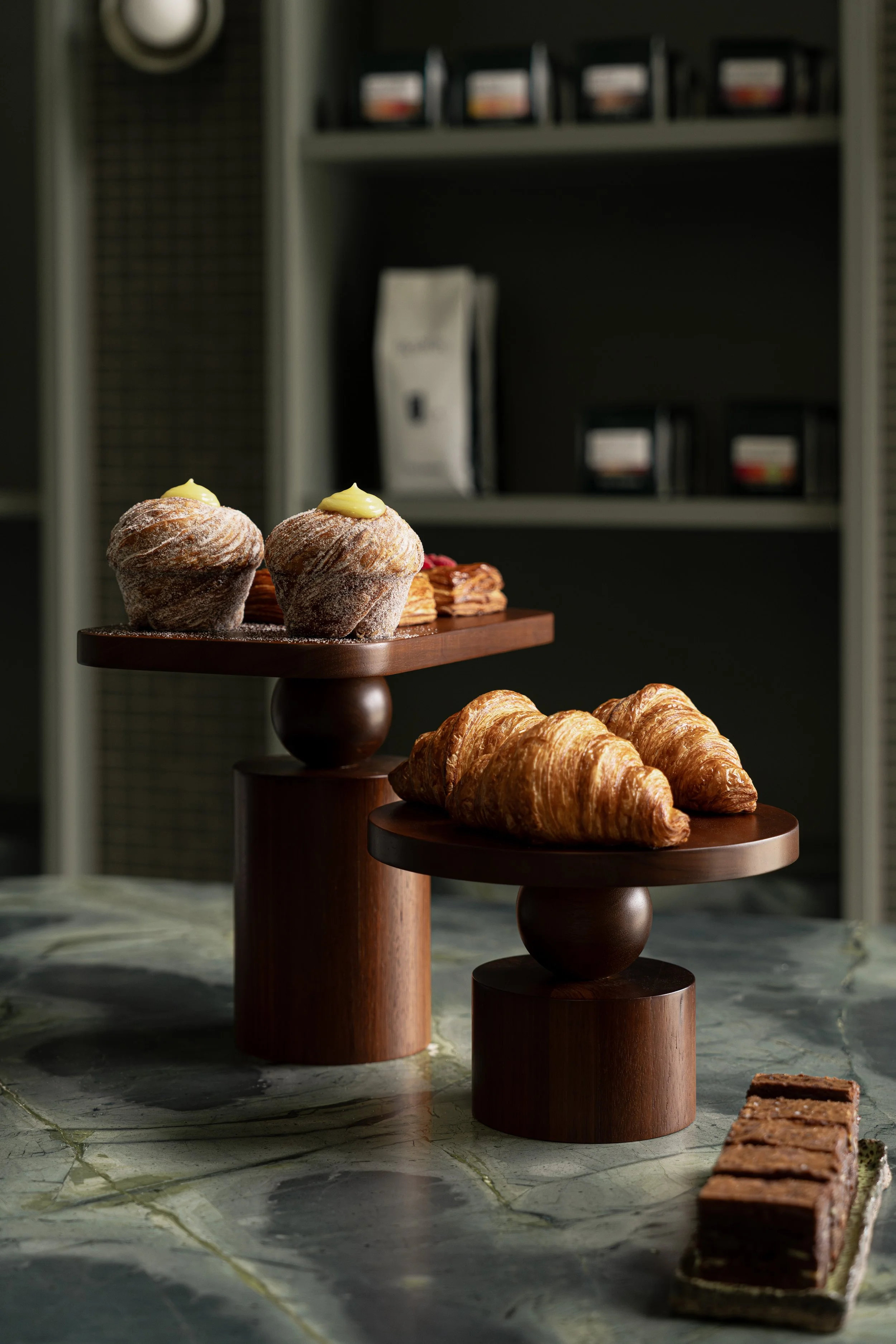 Croissants and muffins on wooden display stands with a bar of chocolate on marble surface.