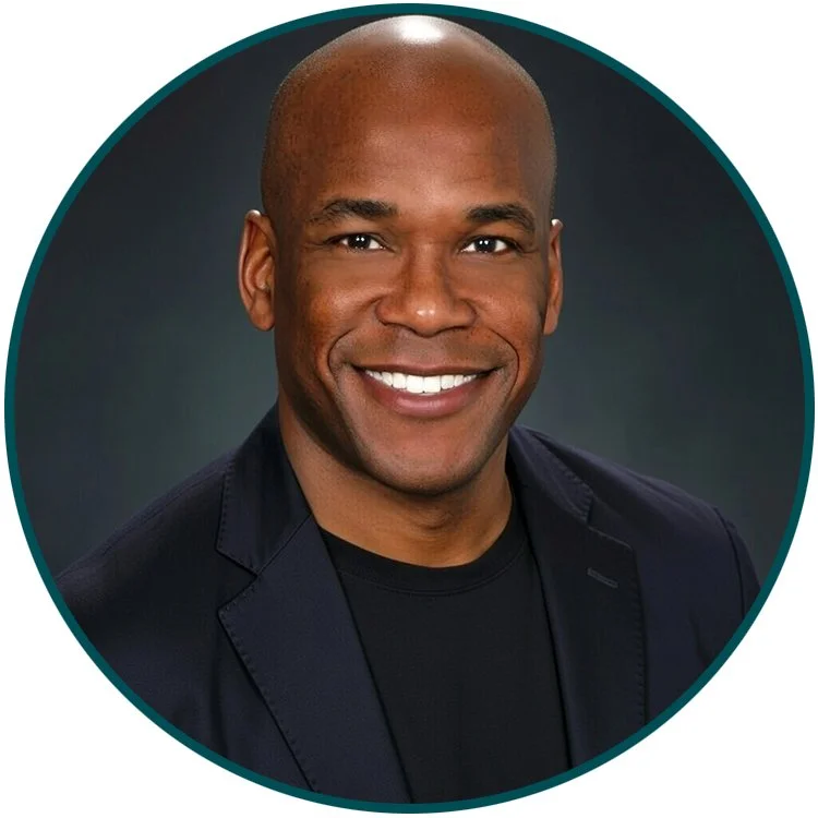 Headshot of a smiling bald African American man wearing a black shirt and a dark blazer against a dark background.