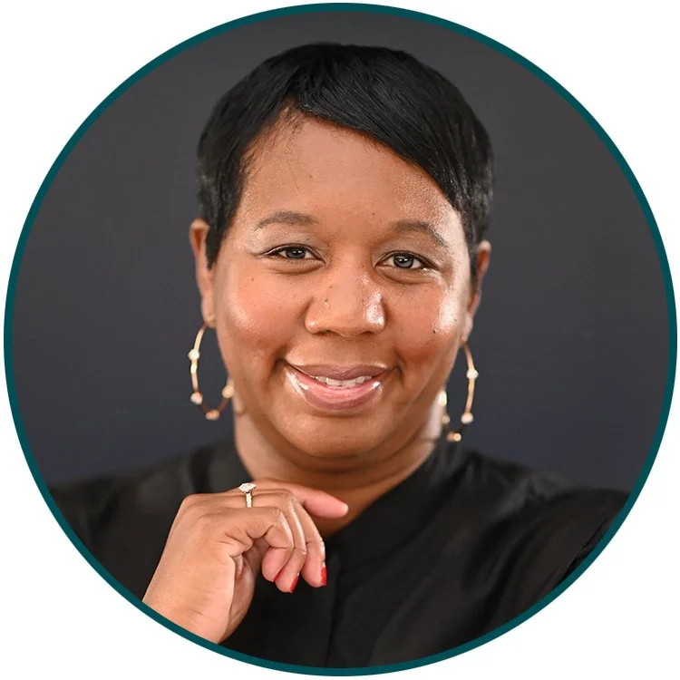 Close-up portrait of a smiling African American woman with short black hair, wearing earrings and a black top, against a dark gray background.