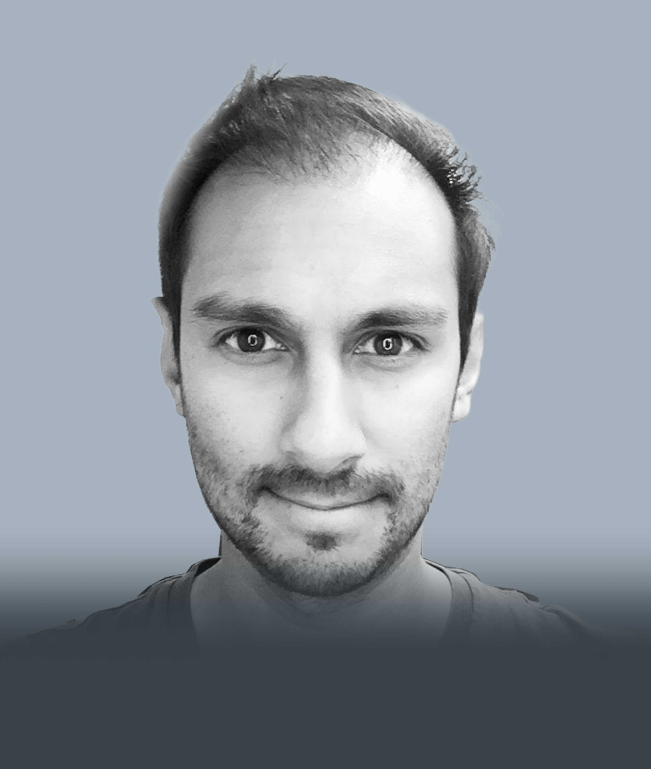 Black and white portrait of a young man with short hair, beard, and mustache, smiling slightly, against a muted grey background.