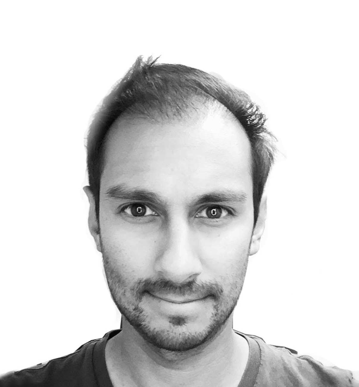 Black and white photo of a young man with short, dark hair, fair skin, faint beard, and mustache, looking directly at the camera with a slight smile. He is wearing a dark shirt.