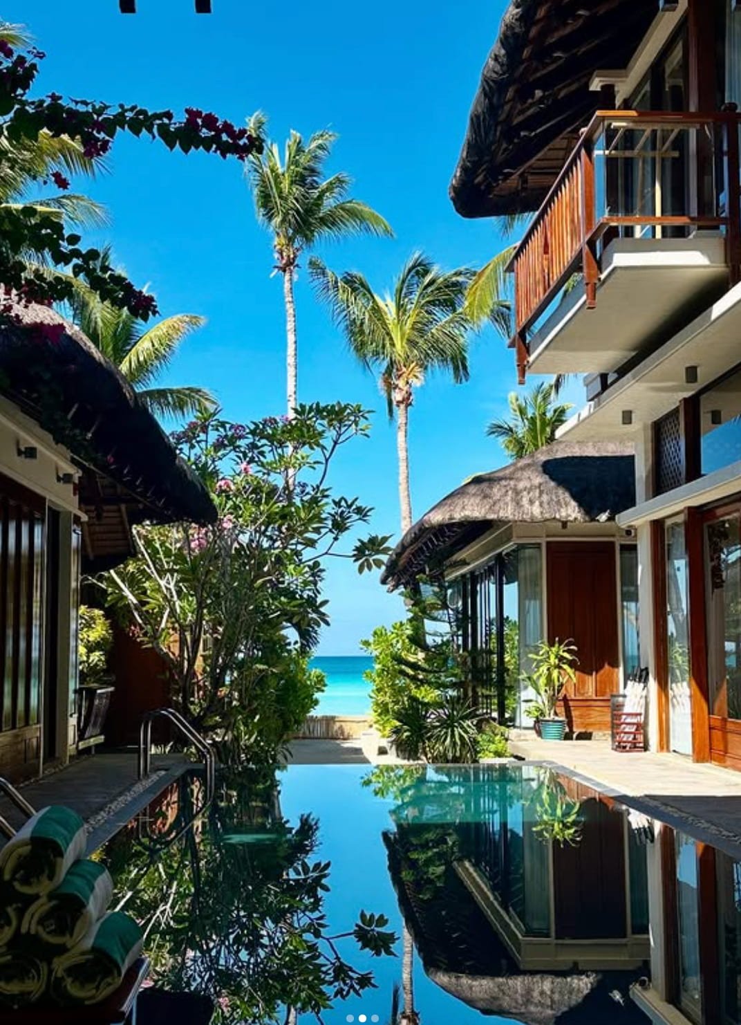 Luxury beachfront villa with a pool, surrounded by tropical plants and palm trees, with the ocean visible in the background under a clear blue sky. Harlan Beach Villa Boracay