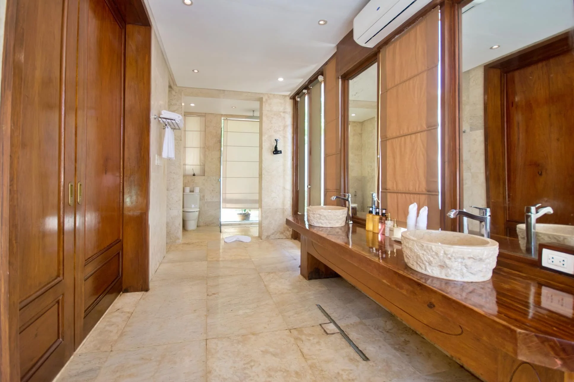 Luxury bathroom with wooden accents, double stone sinks, large mirror, and laundry area in the background. Harlan Beach Villa Boracay