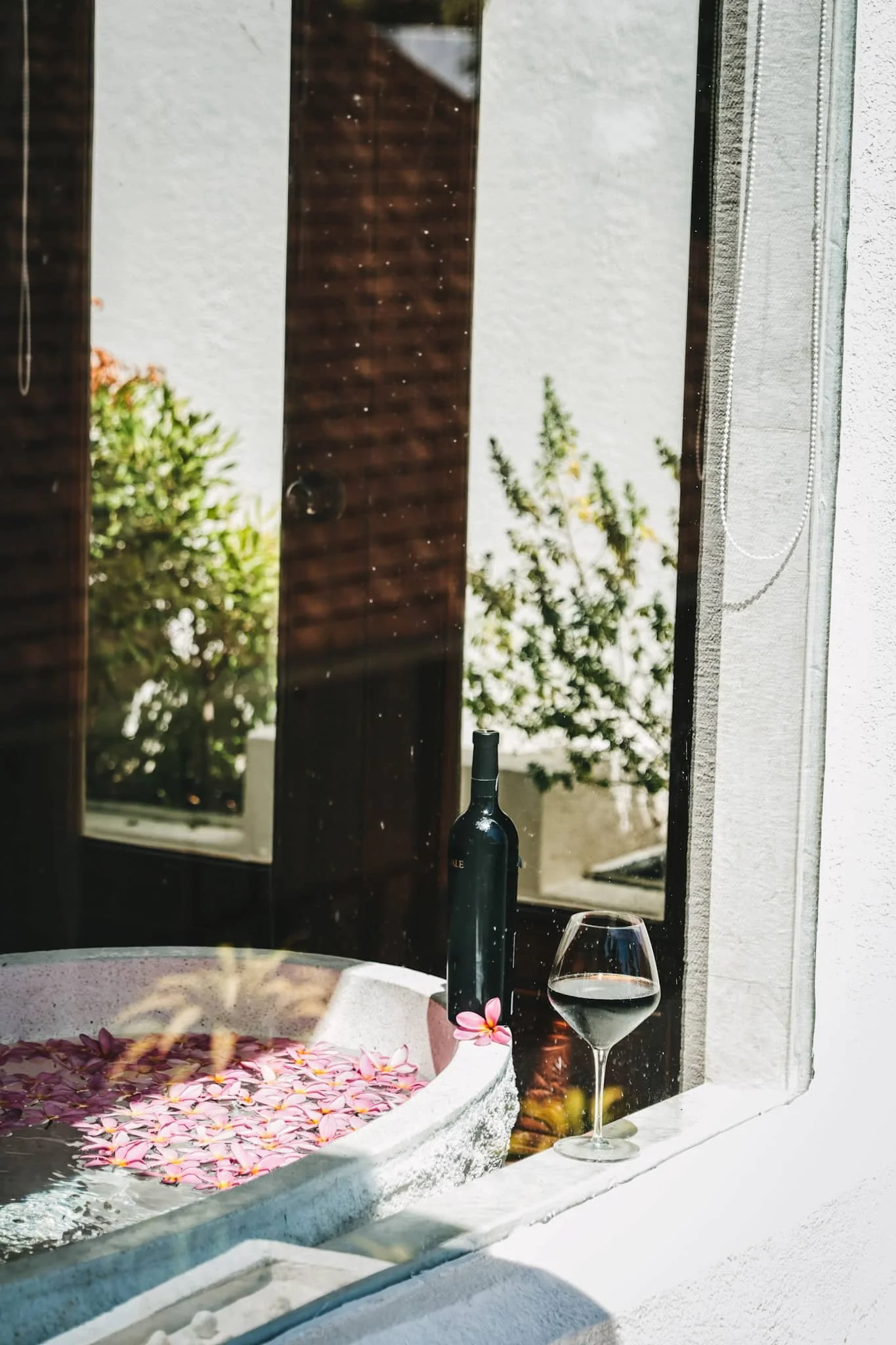 A window with a bottle of wine, a glass of wine, and a small bathtub with pink flower petals inside. Harlan Beach Villa Boracay