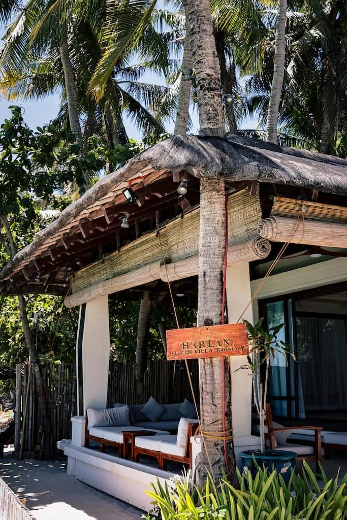 Beach villa with thatched roof, outdoor seating, and tropical trees.  Harlan Beach Villa Boracay