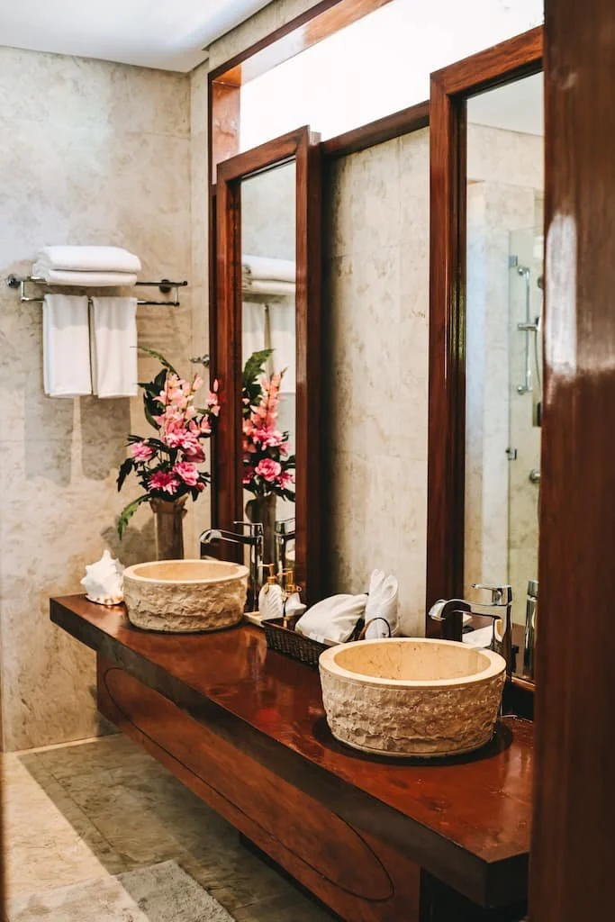 Bathroom with two stone vessel sinks, wooden counter, large mirrors, towels, and pink flowers in a vase. Harlan Beach Villa Boracay