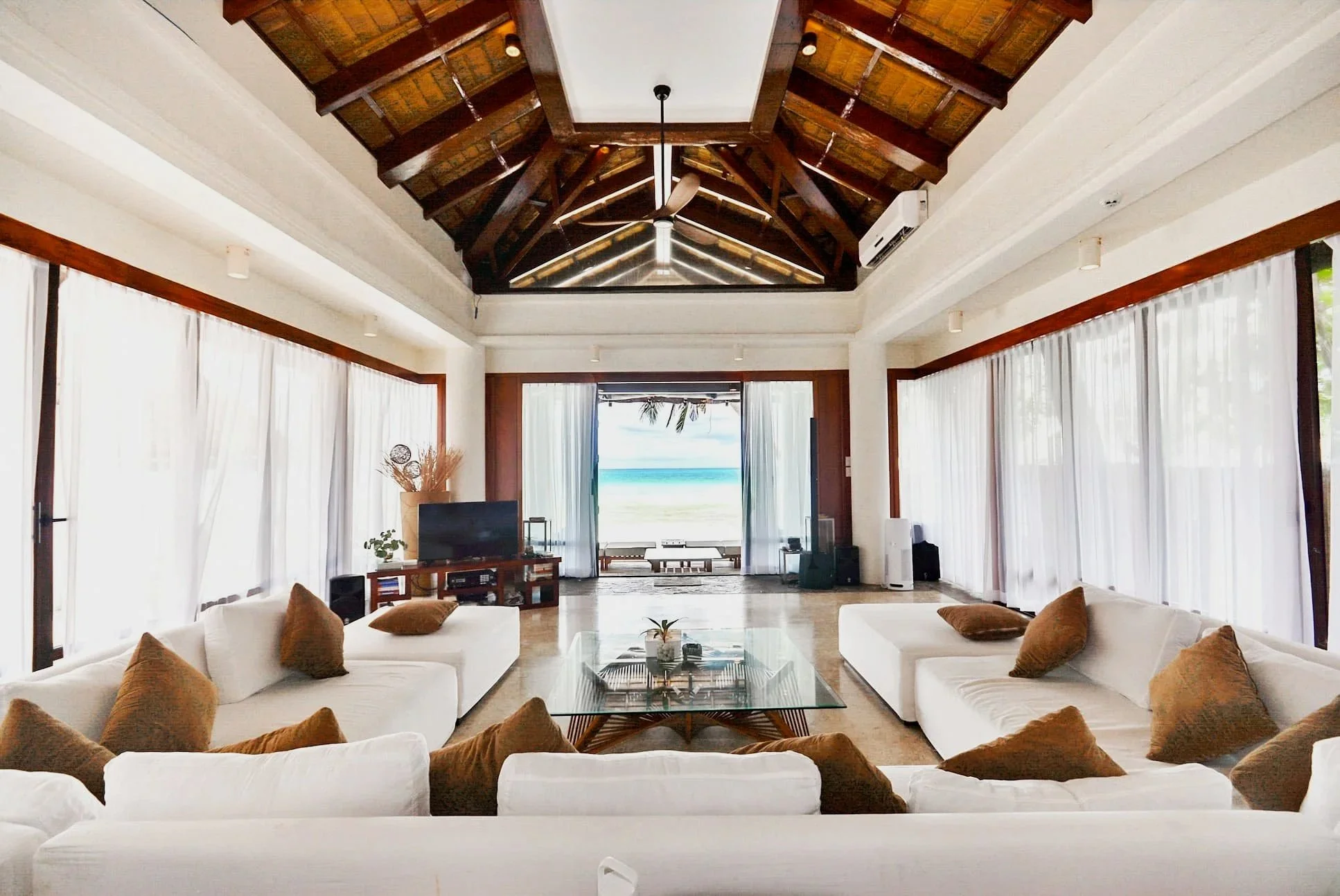 Living room with white sofas, brown pillows, glass coffee table, large windows with white curtains, overlooking a beach and ocean view.  Harlan Beach Villa Boracay