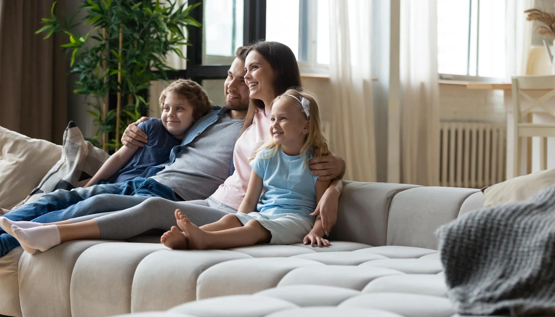A family of four sitting on a white sofa in a living room, smiling and enjoying each other's company.