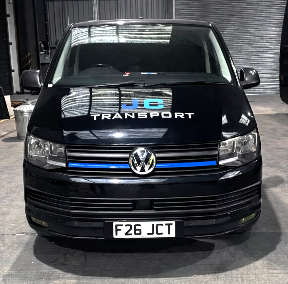 Black Volkswagen van with JC Transport logo on the hood, parked indoors, with a license plate reading F26 JCT.