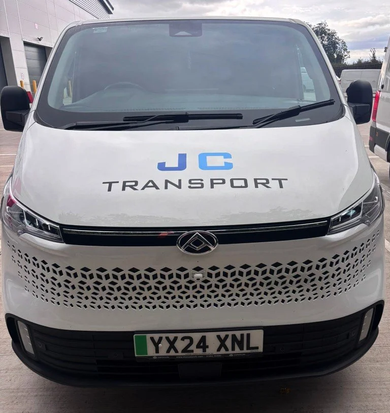 Front view of a white van with J C TRANSPORT written on the hood and a European license plate reading YX24 XNL.