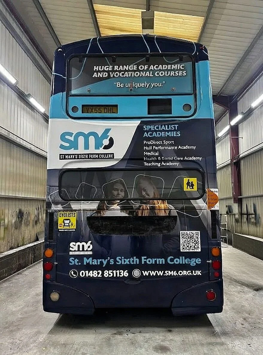 The rear of a bus for St. Mary's Sixth Form College, featuring various advertisements and information about courses, with a couple of students' images and the college's contact details.