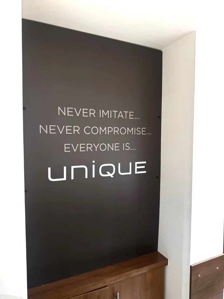 Inspirational quote wall with dark gray background and white text that reads: 'Never imitate... Never compromise... Everyone is... unique'.