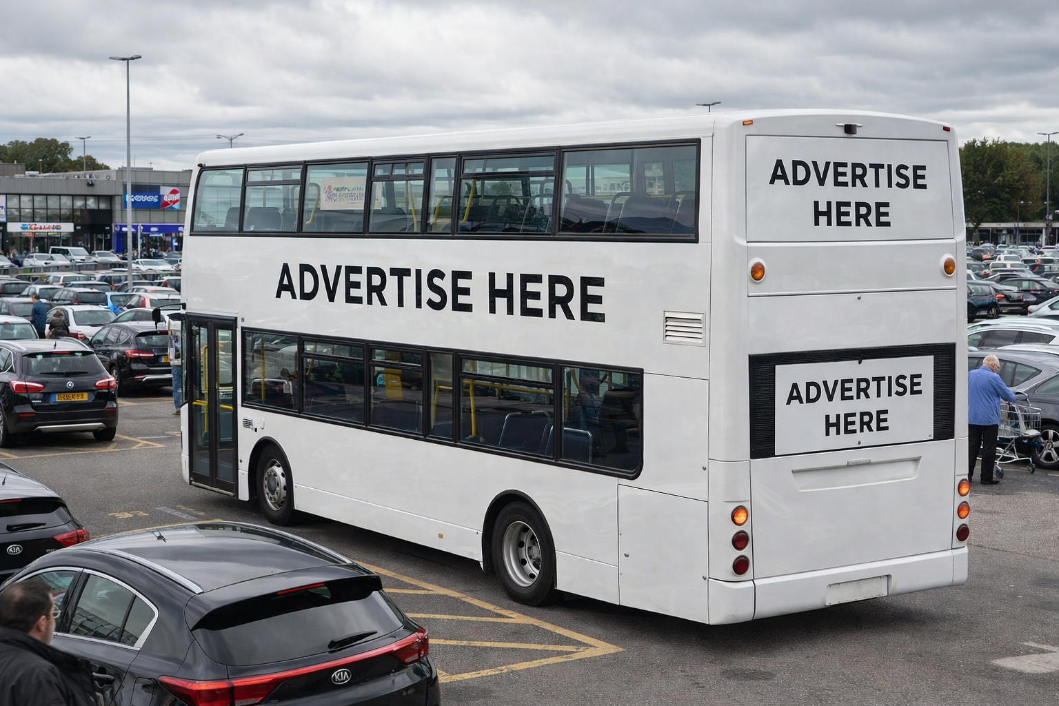 A white double-decker bus in a parking lot with large signs on it that say 'ADVERTISE HERE' in black letters.