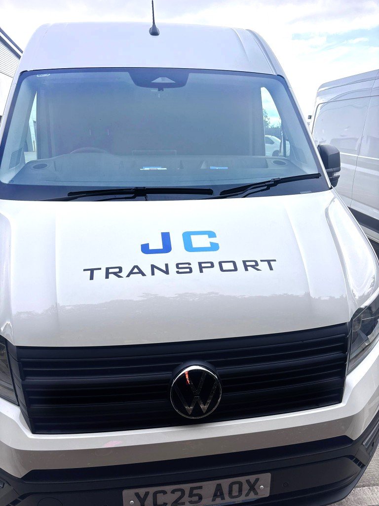 Front view of a white Volkswagen transport van with JC Transport written on the hood and a license plate YC25 AOX.