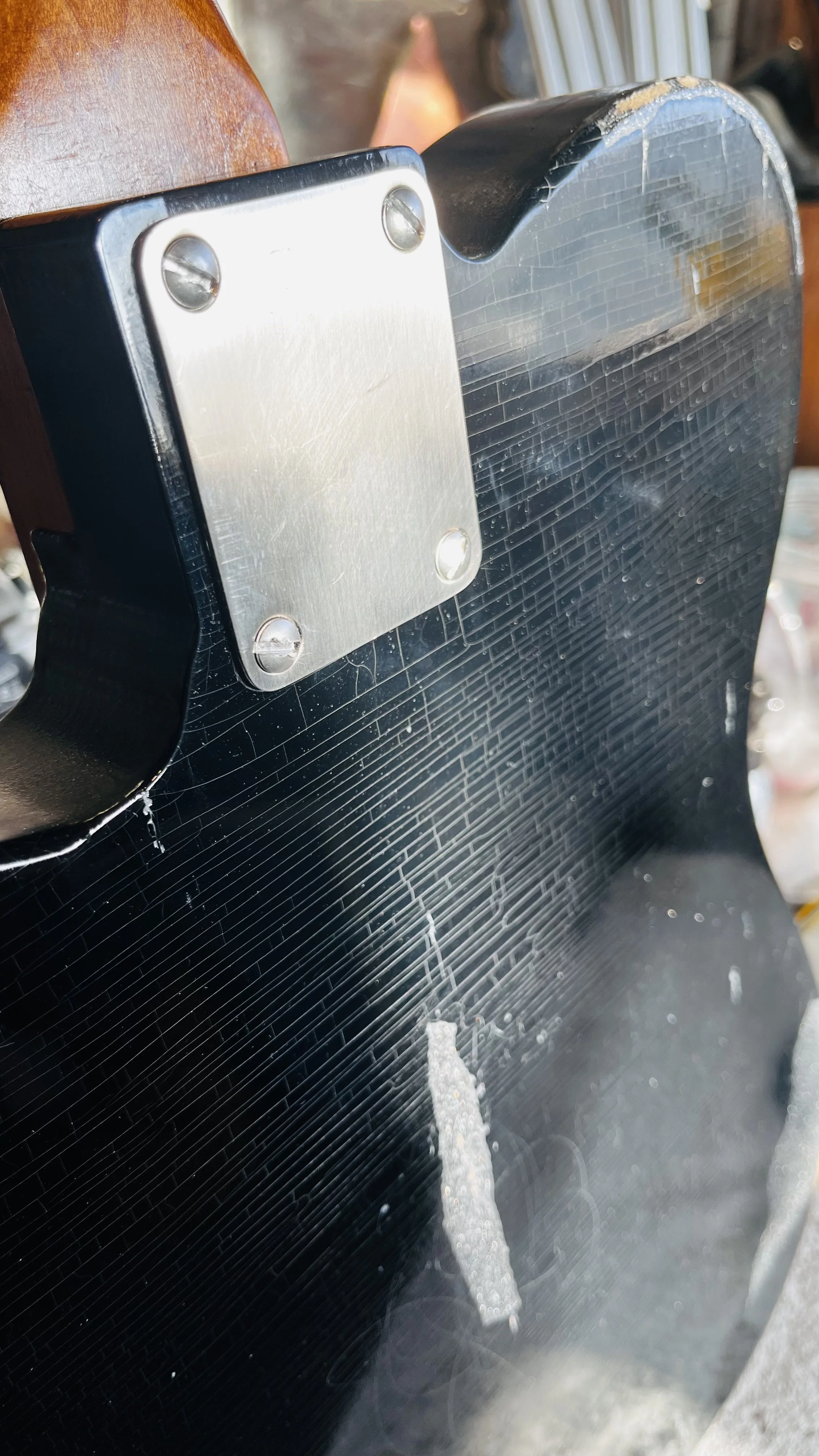 Black object with a silver metal plate attached by four screws, part of a machine or device, with a textured or patterned surface and some visible damage or wear.