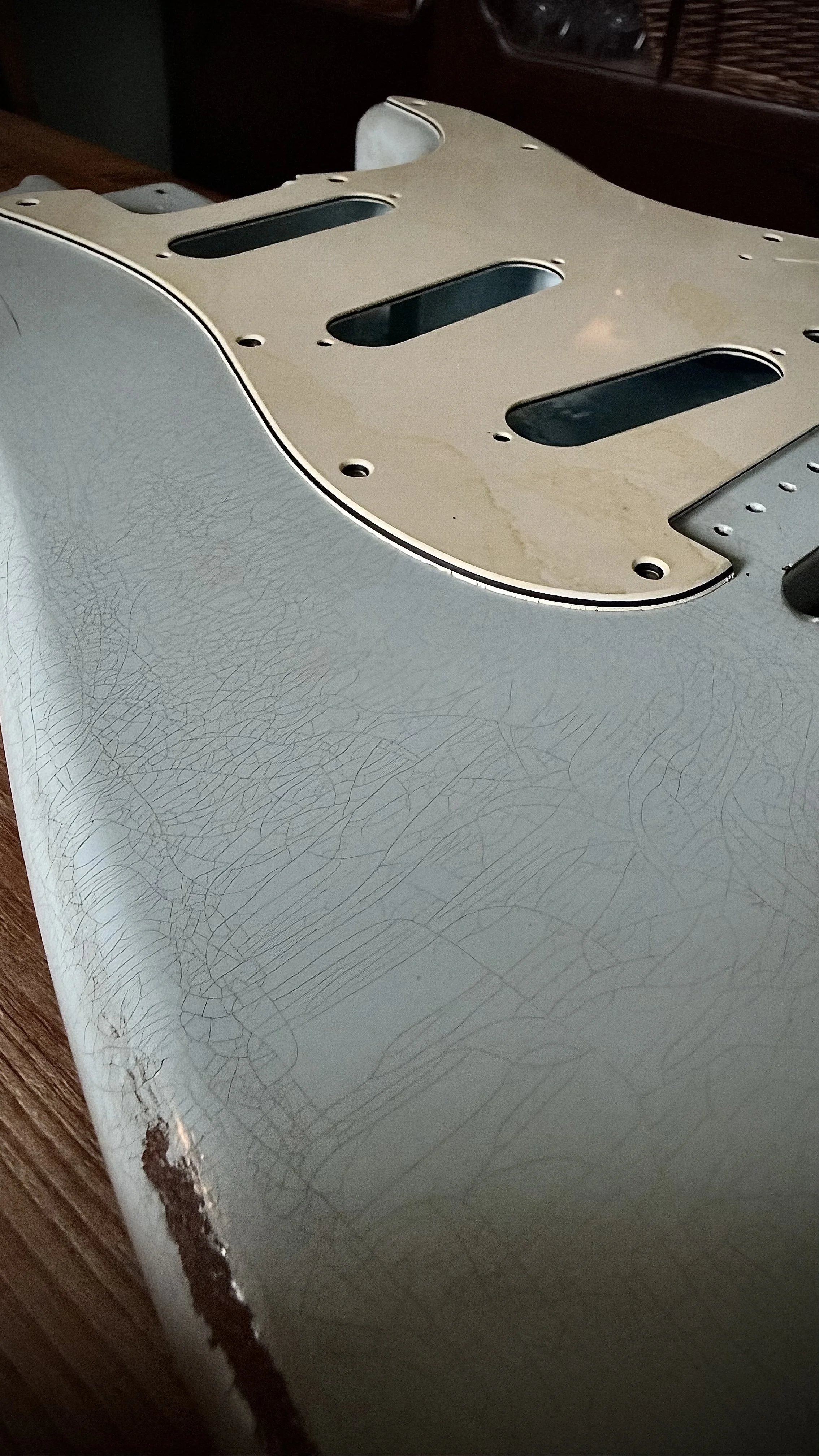 Close-up of a vintage electric guitar body with a crackled white finish and a worn, discolored pickguard.