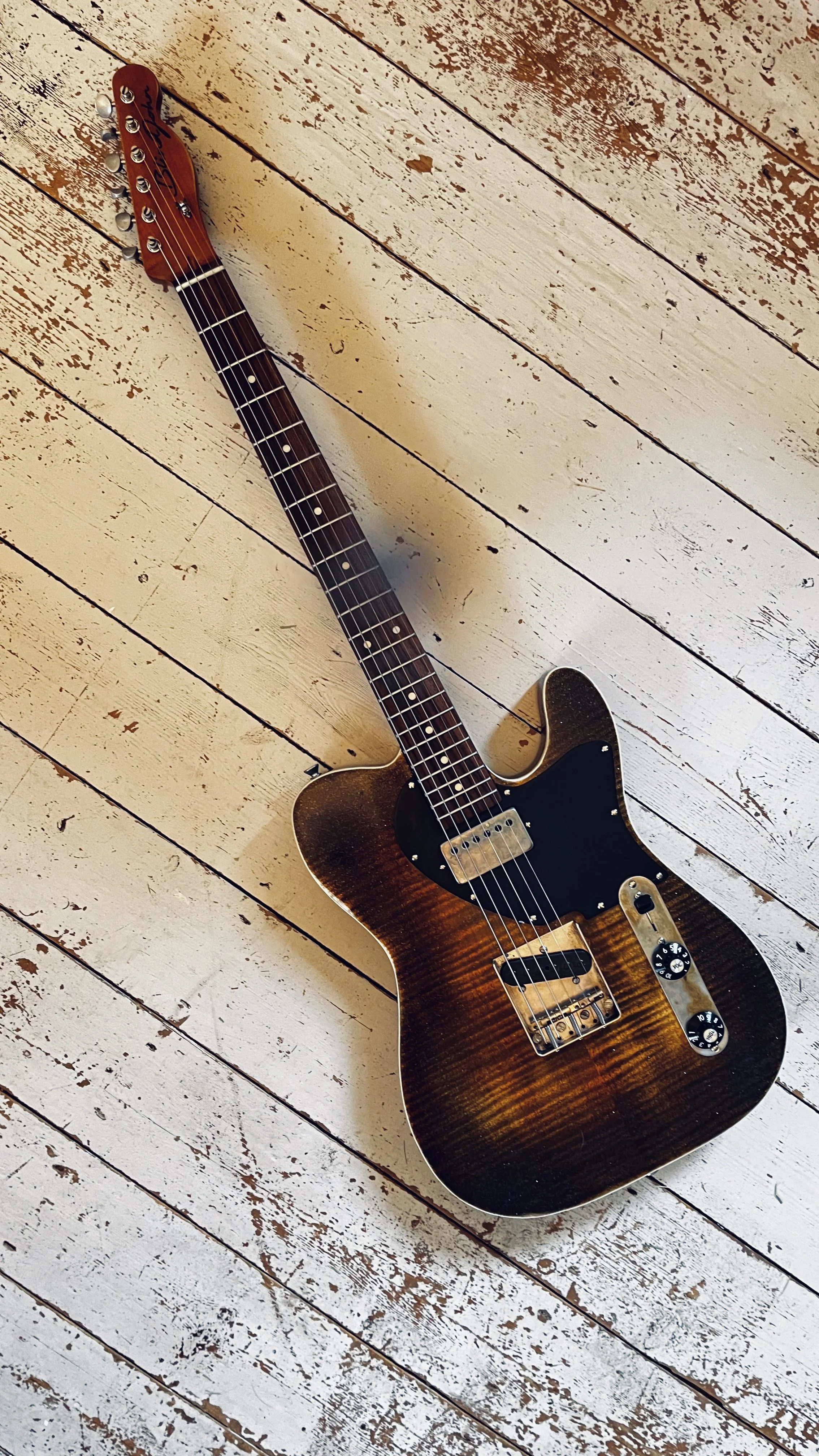 A vintage electric guitar with a sunburst finish on a distressed white wooden floor.