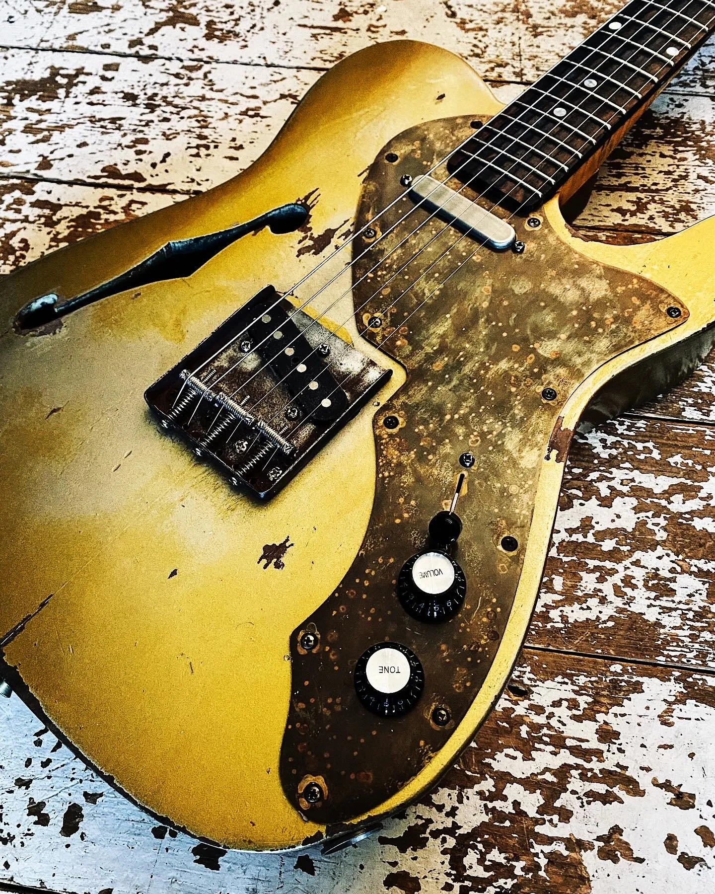 A vintage yellow electric guitar with signs of wear, placed on a distressed wooden surface.