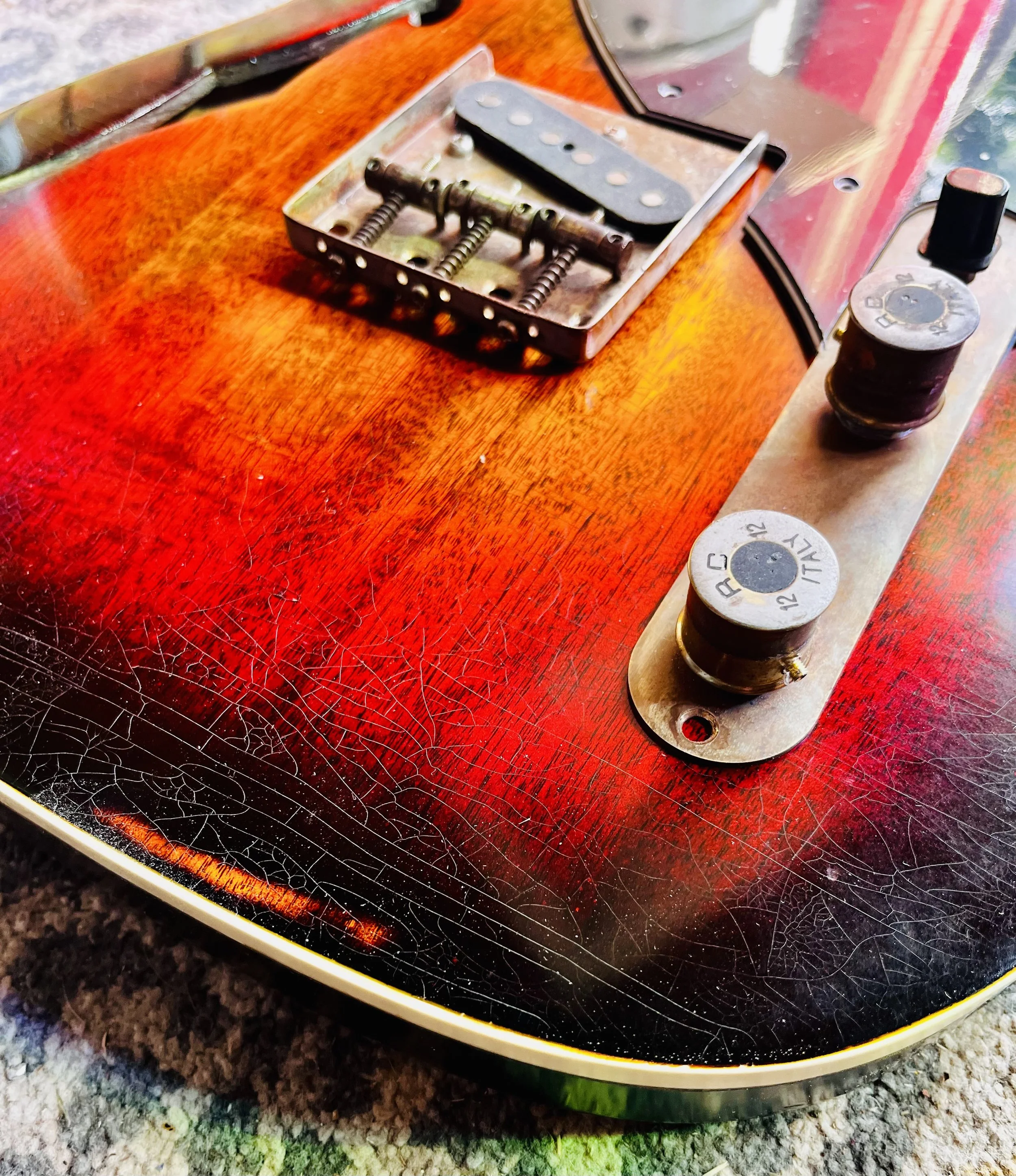 Close-up of a vintage electric guitar with a cracked and worn red and black finish, showing the bridge, knobs, and part of the body.