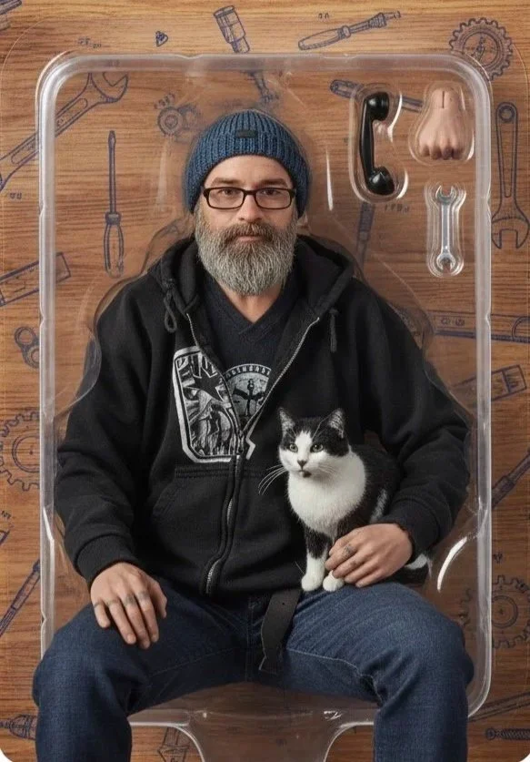 A man with glasses and a gray beard wearing a blue beanie and black hoodie sitting inside a clear plastic container with a black and white cat on his lap, on a wooden surface with drawings of tools.