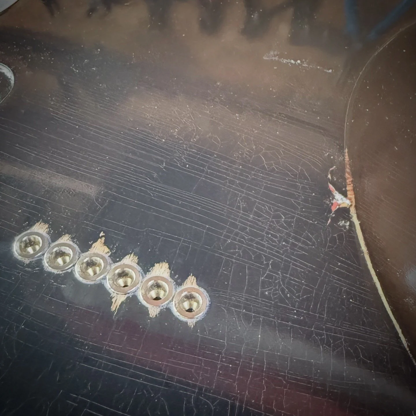 Close-up of scratched and worn black surface with six silver screws near the bottom left corner and some chipped area on the right side.