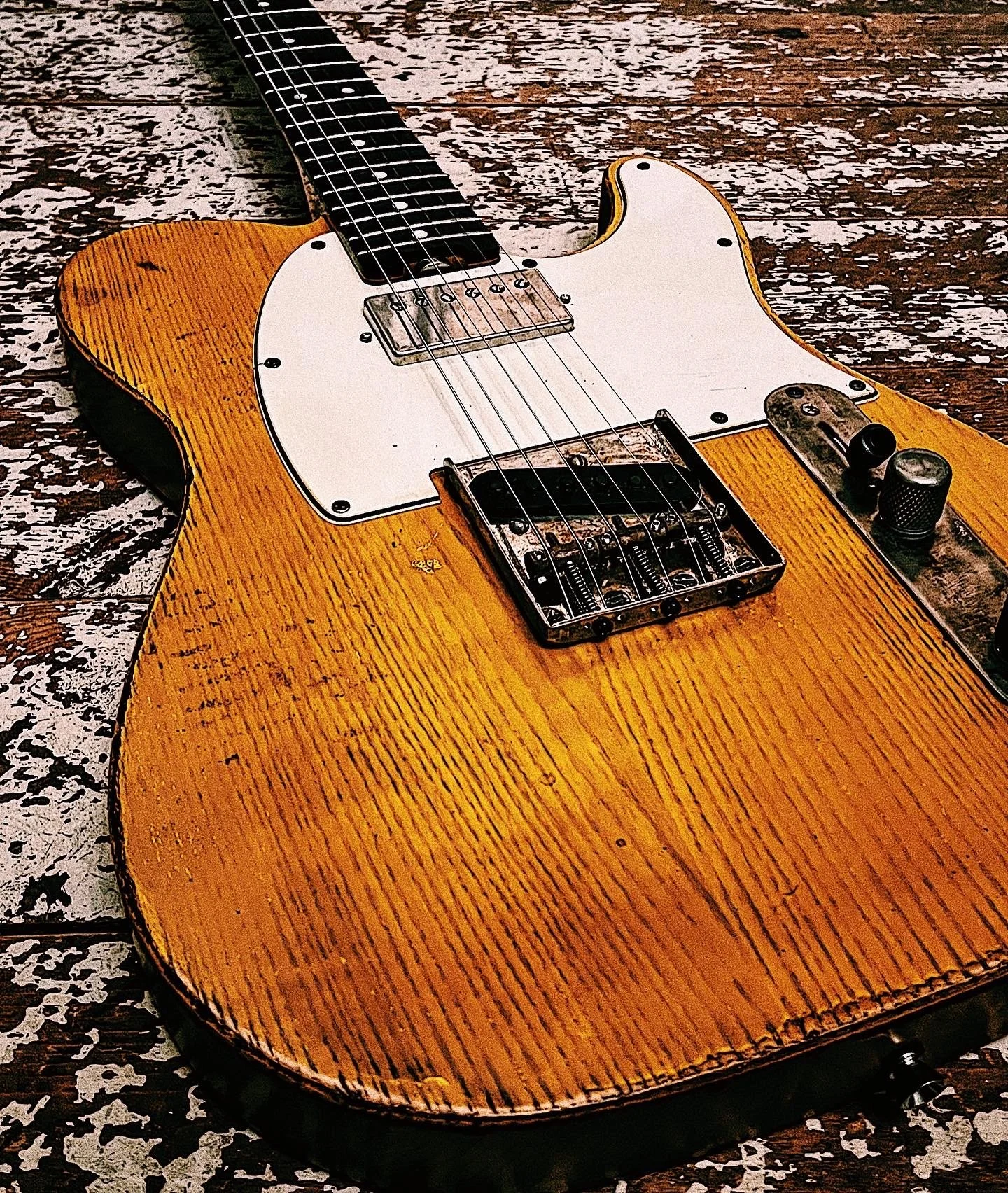 A vintage electric guitar with a worn wooden body, white pickguard, bridge, and control knobs, lying on a distressed wooden surface.