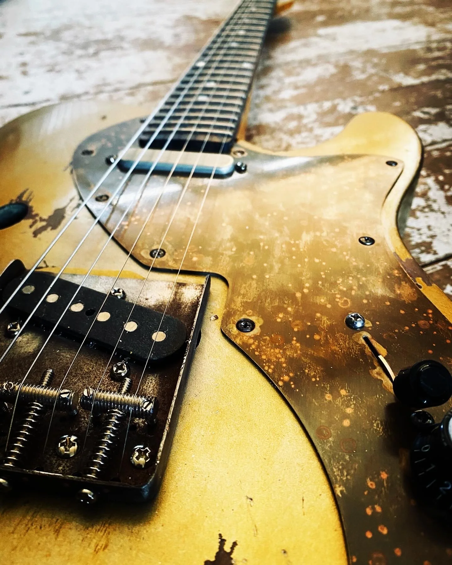 Close-up of a vintage electric guitar with worn yellow paint and rust spots on the pickguard, lying on a wooden surface.