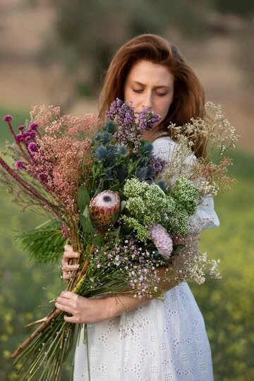 Woman in white dress holding a large bouquet of various flowers outdoors.