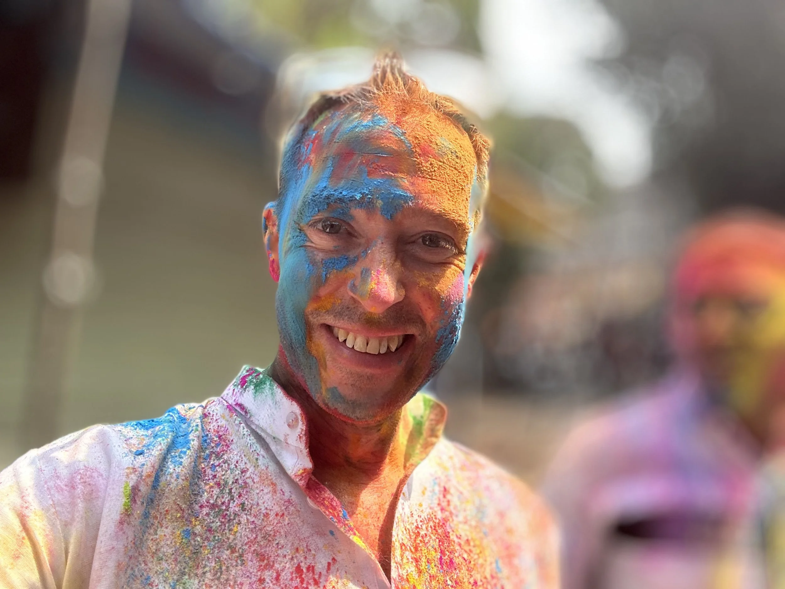 Rob Hales smiling with face and shirt covered in colourful powder during the Holi festival.